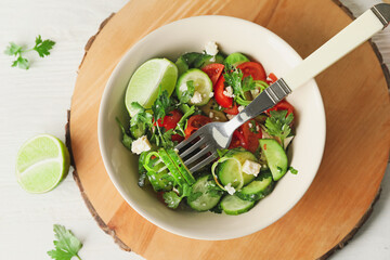 Bowl of fresh salad with vegetables on light wooden background