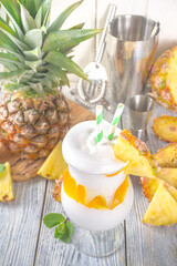 Modern Tropical Lava Flow Cocktail. Sweet and delicious summer drink with pineapple, rum and coconut cream. With sliced pineapple and bar utensils, on wooden background 