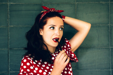 Young beautiful woman dressed in retro style. The girl looks thoughtfully aside, gnaws at the bow of the glasses