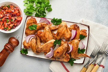 Grilled chicken wings or roasted bbq with spices and tomato salsa sauce on plate on a light grey slate, stone or concrete background. Top view with copy space.