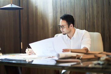 Asian bearded designer sitting, thinking and sketching ideas indoors
