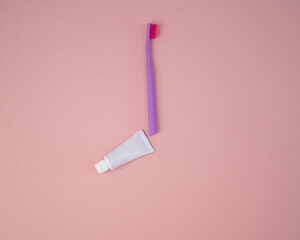 Toothbrush and a tube of toothpaste on a pink background. Oral hygiene products