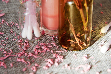 Tiny glass jar with cotton buds, pink lip gloss and scented flower petals. Makeup desk. Fashion...