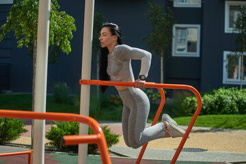 A young woman goes in for sports on the sports ground, performs push-ups on the uneven bars. Side view.