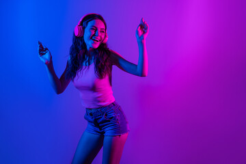Photo of young smiling excited funky woman look copyspace dancing in headphones isolated on neon blue color background