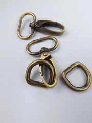 Haberdashery accessories, metal snap hooks or metal swivel clip snap hooks and D rings for bag strap, all in brass color. Isolated against white background. 