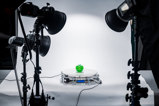 A rotating table for subject photography, with a plastic green apple on it, on a table in a photo studio.