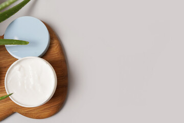 Opened container with cream and aloe on the wood on grey background. copy space