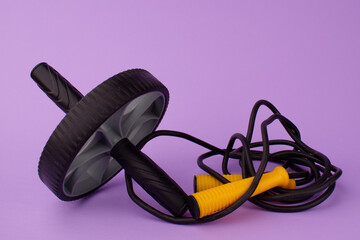 A gym wheel and skipping rope on a purple background. Press wheel. Sports at home remotely. Home fitness and exercise concept.