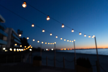 Close up of the glowing light bulbs at the beach cafe terrace. Sun is setting in the blurry abstract background.