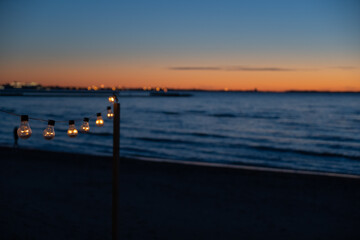 Obraz premium Close up of the glowing light bulbs at the beach cafe terrace. Sun is setting in the blurry abstract background.