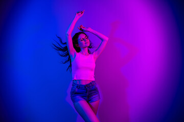 Photo of adorable positive girl closed eyes raise arms enjoy vacation disco isolated on neon...