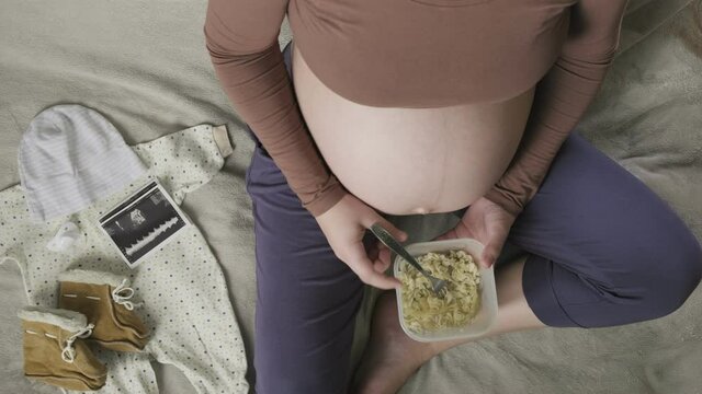 Top vew of expecting pregnant woman with large belly eating pasta at home