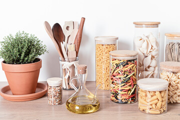 Assortment of pasta in glass jars, olive oil, vegetables and kitchen utensils on wooden table. Italian ingredients, healthy balanced food, sustainable lifestyle, zero waste eco friendly concept