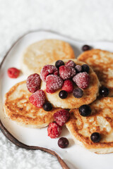 Best view of ceramic plate with cheese cakes, raspberries and currants on a white blanket. Close up. Breakfast concept
