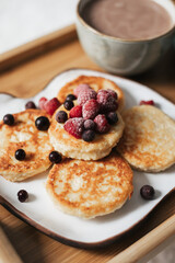 Cheesecakes with berries, a mug of cocoa on a tray against a white plaid background. Close up. Breakfast concept
