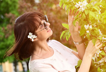 Naklejka premium beautiful woman in sunglasses with dark hair among the white flowers of a blooming apple tree. Artistically colored and tinted photography