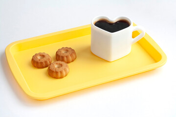 A heart-shaped cup with coffee and cookies on a yellow tray