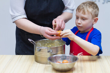 A boy in a red apron prepares dough and breaks eggs into a pot at a master class