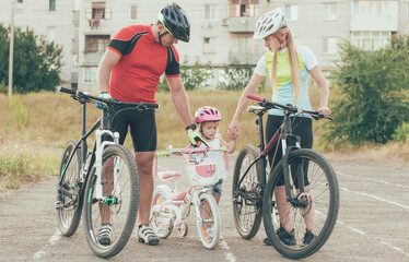 Fototapeta premium Mom and Dad are teaching little daughter to ride a bike in the stadium