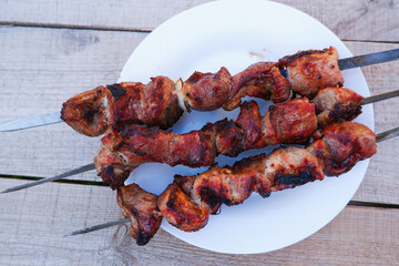 Juicy meat on skewers on a white plate on a wooden background. Kebab of meat is fried on the grill.