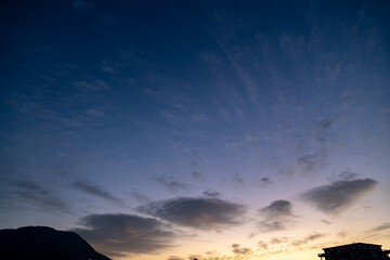 Dusk night sky background. Sun set over mountains and wind scattered smal clouds over the horizon.