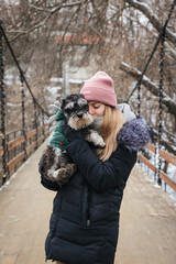 Caucasian woman hugs a small black dog on the bridge in winter. Little puppy zwergschnauzer with its owner. Friendship and family concept
