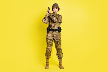 Full size portrait of concentrated military girl standing hands hold pistol isolated on yellow color background