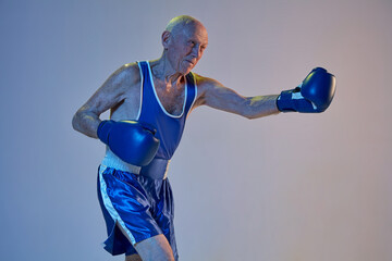 Senior man wearing sportwear boxing isolated on gradient studio background in neon light. Concept...
