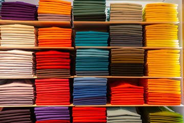 Clothes folded in a shelve and organized by colour ranges