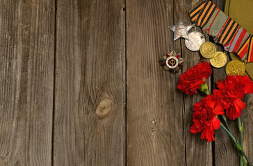 Victory Day.Order of the red star and medals with the Russian inscription Patriotic waron a wooden background with red carnations.Celebration on may 9.Memorial day.Greeting card.copy space