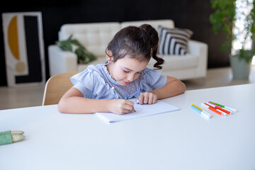 Beautiful young schoolgirl drawing at a white table in her room, home learning concept