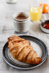 Breakfast with croissant, jam and hot chocolate, juice and tangerine on greige linen tablecloth. Selective focus