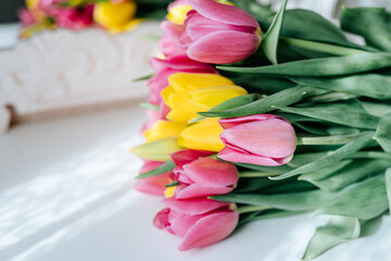 Obraz premium Fresh spring yellow and pink tulips bouquet on white wood table background with copy space for text. Love, easter, International Women day, Mother day and Happy Valentine day concept