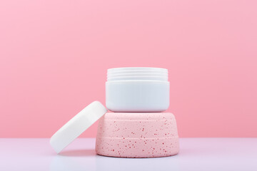 White opened cosmetic jar on pink podium against bright pink background. Face creme, mask or scrub...