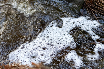 White foam on the water in the river near the shore. Close-up.