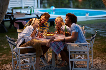 group of multiethnic friends laughing, gathered, sitting at the table by the pool