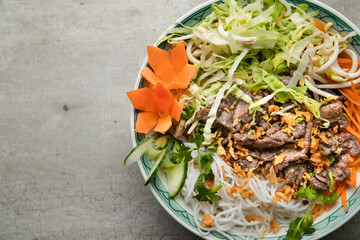 A large bowl of traditional South Vietnamese noodle dish called Bun Bo Nam Bo with beef, noodles, fresh herbs, pickled vegetables and fish sauce.