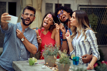 Cheerful couples using funny accessories for selfie at the open air birthday party. Quality friendship time together