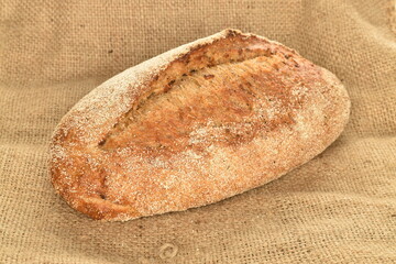 One fresh loaf of bread on craft paper, close-up, on a jute fabric.