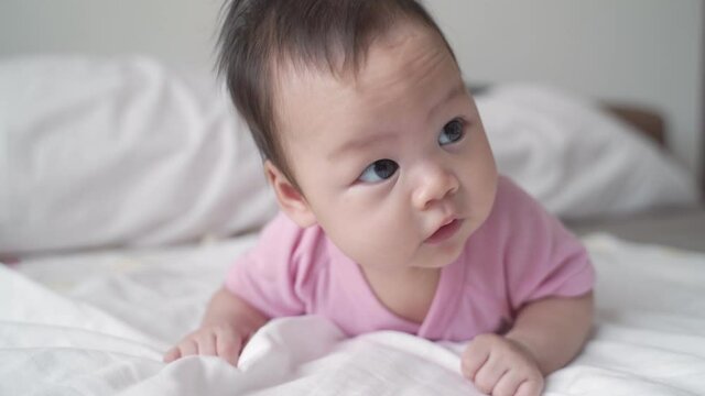 happy asian baby infant learning to crawl on white soft bed. 3 months old baby facial expression. lovely and smile baby..