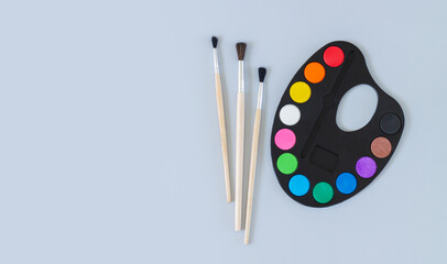 Art palette with paint and brushes top view on gray background