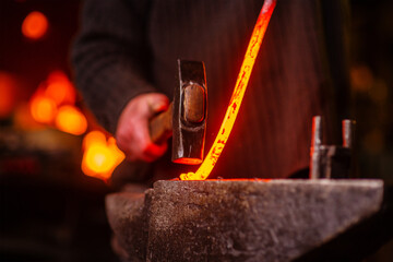 A close-up image of a blacksmith's hands forging a spiral from a red-hot billet against the background of a forge. Handicraft concept