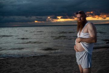 Humorous portrait of a brutal man posing on the beach at sunset