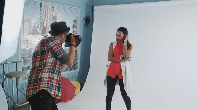 Behind the scenes on photo shoot: professional photographer working in studio by taking photos of black model