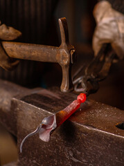 A close-up image of a blacksmith's hands forging a jewelry flower from a hot sheet of metal. Manual rework in the forge concept