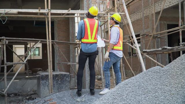 back view asian foreman and african american architect discuss with blueprint outdoor on construction site at village. contractor worker Inspection with builder. Engineer and foreman. quality control