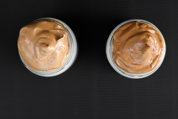 Two jars of  coffee cream on black background. Whipped cream coffee close up. 