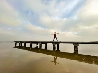 Young woman practices yoga on a lake with cloudy sky