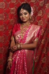 Portrait of an beautiful woman Indian model in Bridal look with heavy gold jewelry and red sari.